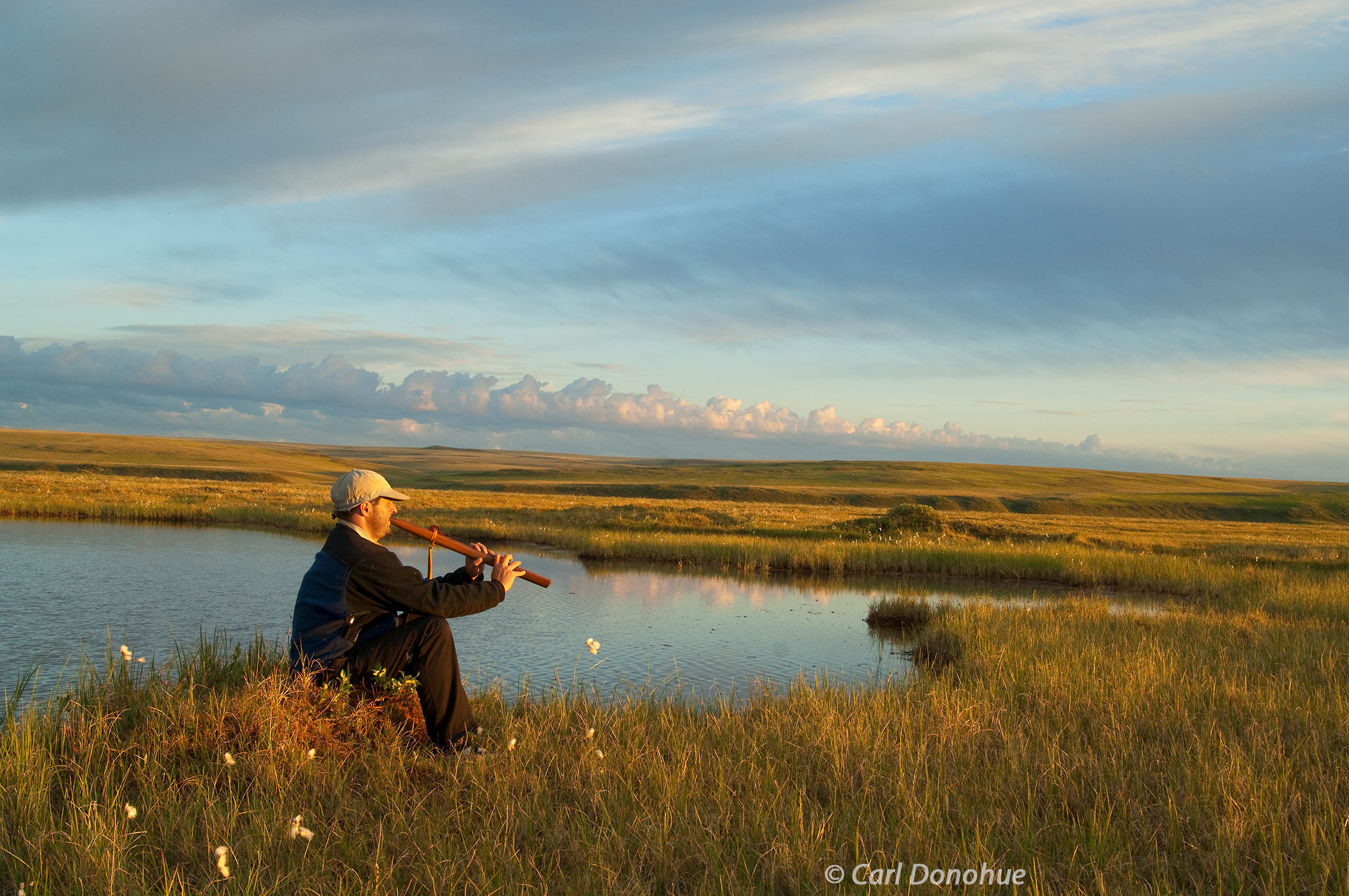 A hiker sits and plays music on a Native American traditional flute on the coastal plain of the Arctic National Wildlife Refuge...