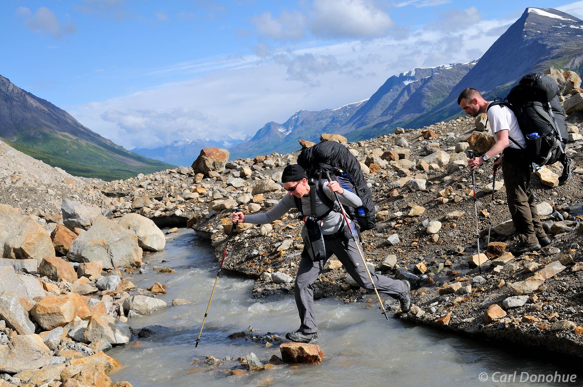 Backpackers crossing a small stream on the Tana Lobe of the bremner Glacier, in the Chugach Mountains. The Chugach extend into...