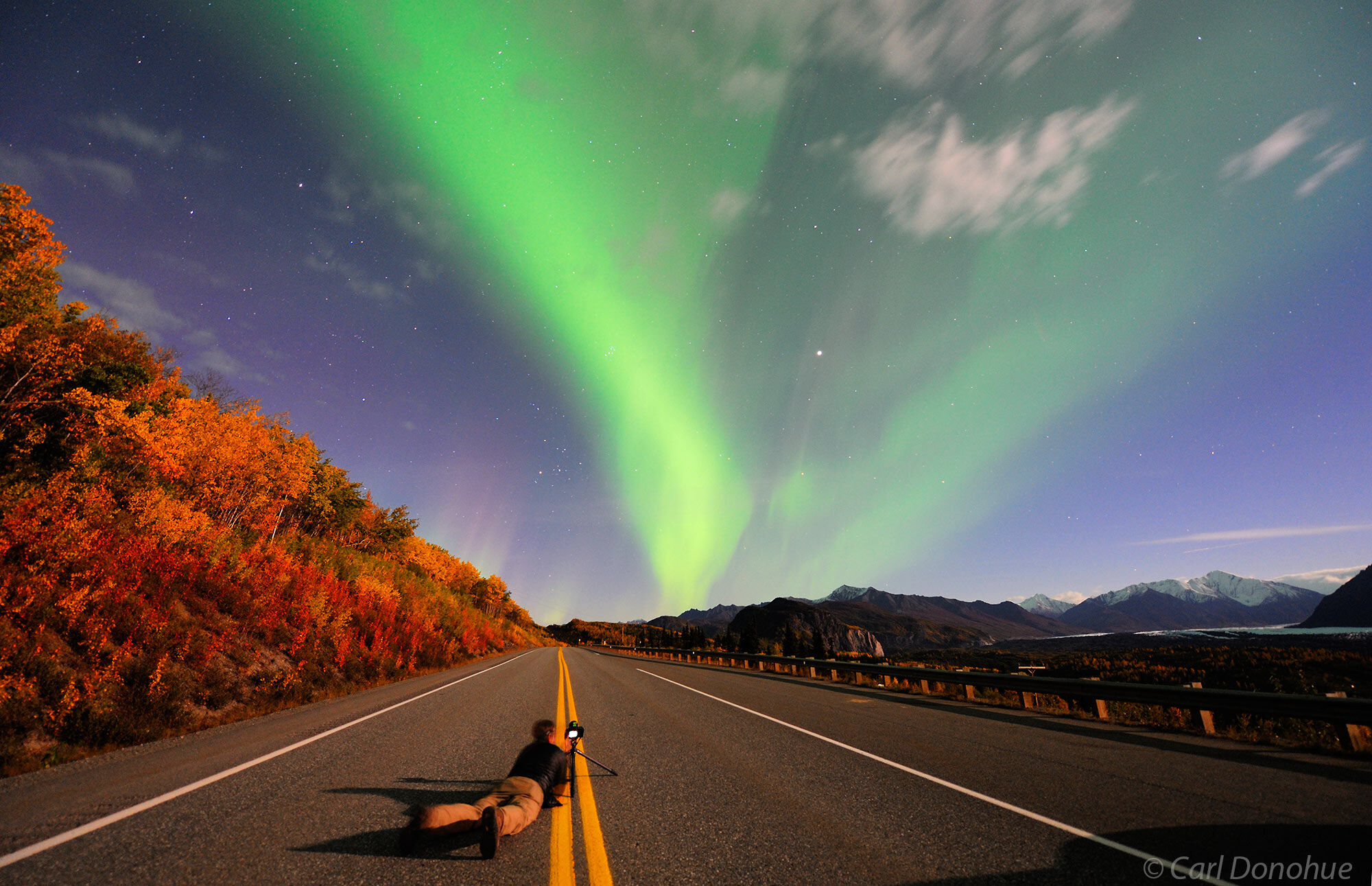 A photographer prone on the ground on the Glenn Highway photographs the Northern lights as they light up the night sky and fall...