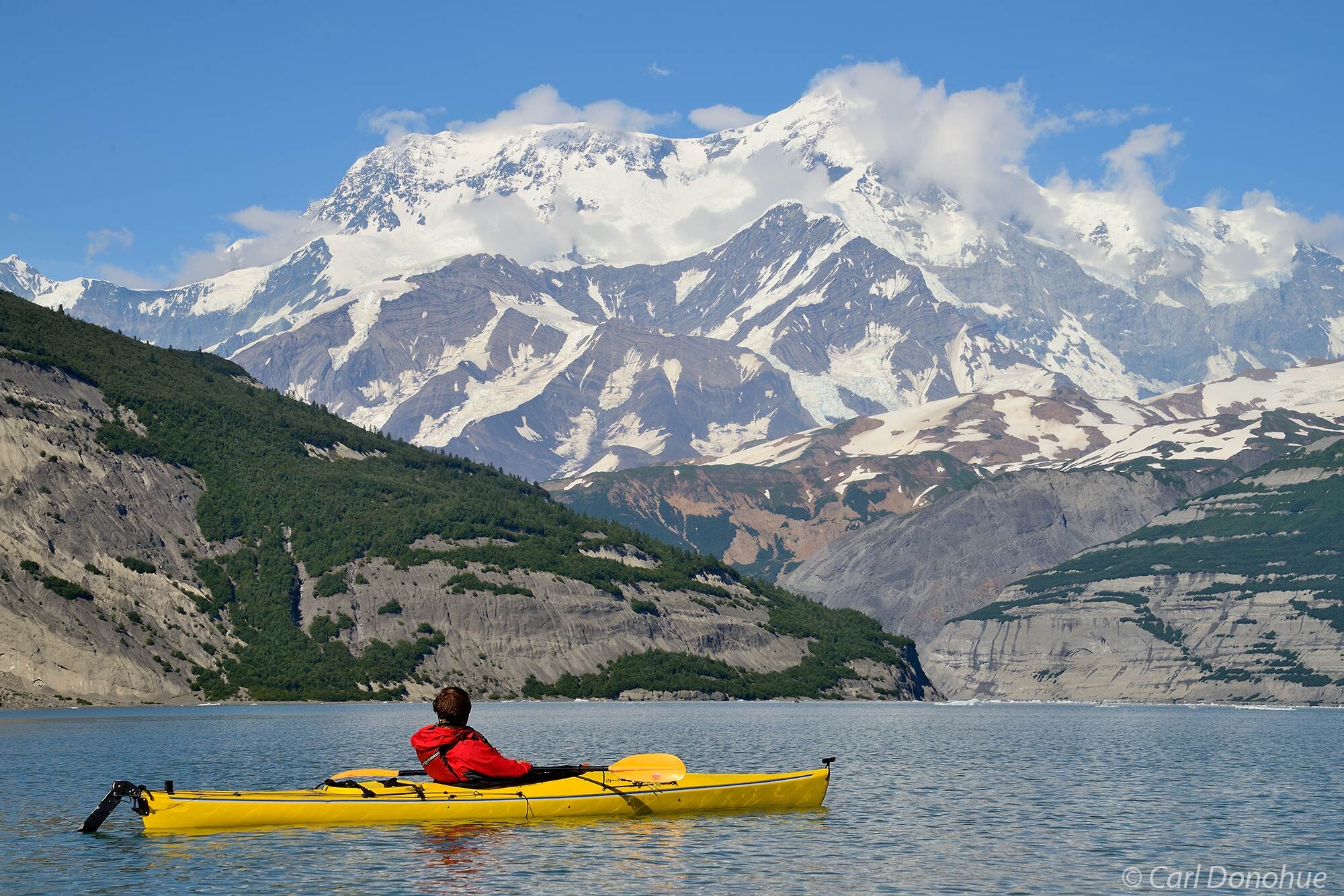 A photo of a young man sea kayaking in Icy Bay admiring the towering Mt. St. Elias. Paddling under the world's highest coastal...