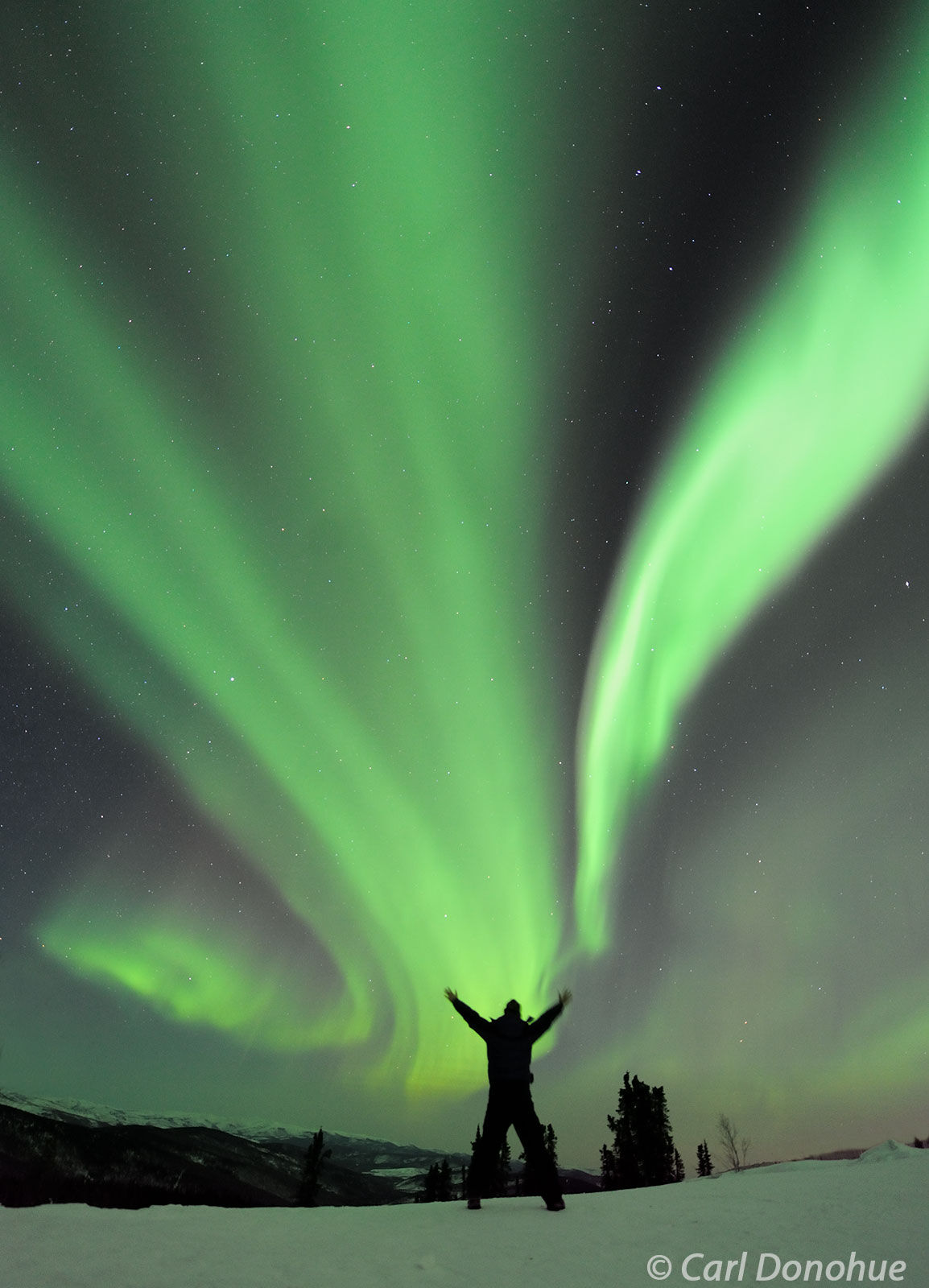 Photo of a person silhouetted against the northern lights, Alaska.