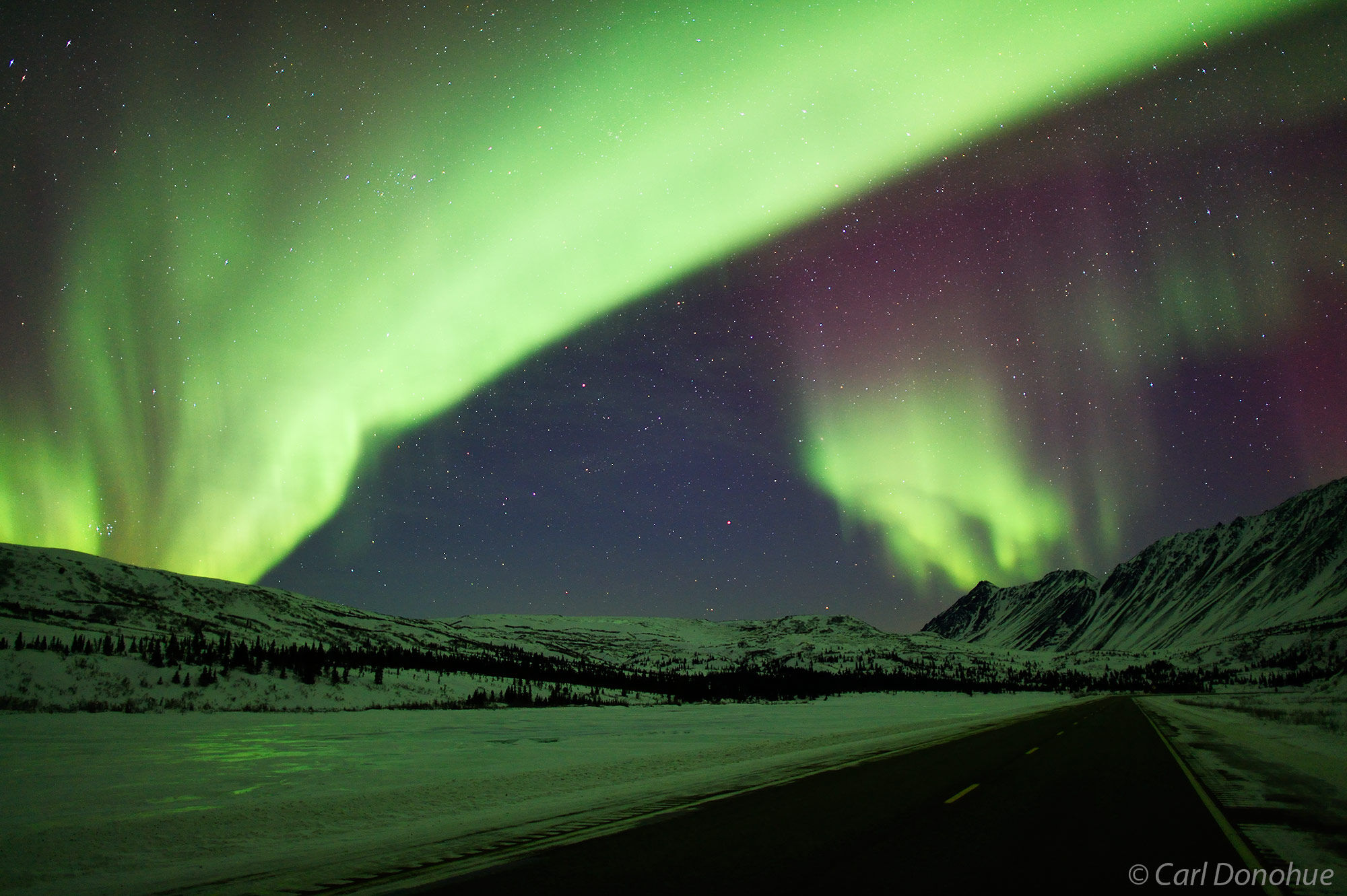 A photo of the northern lights crossing the highway as it cuts through central Alaska?s Alaska Range mountains.