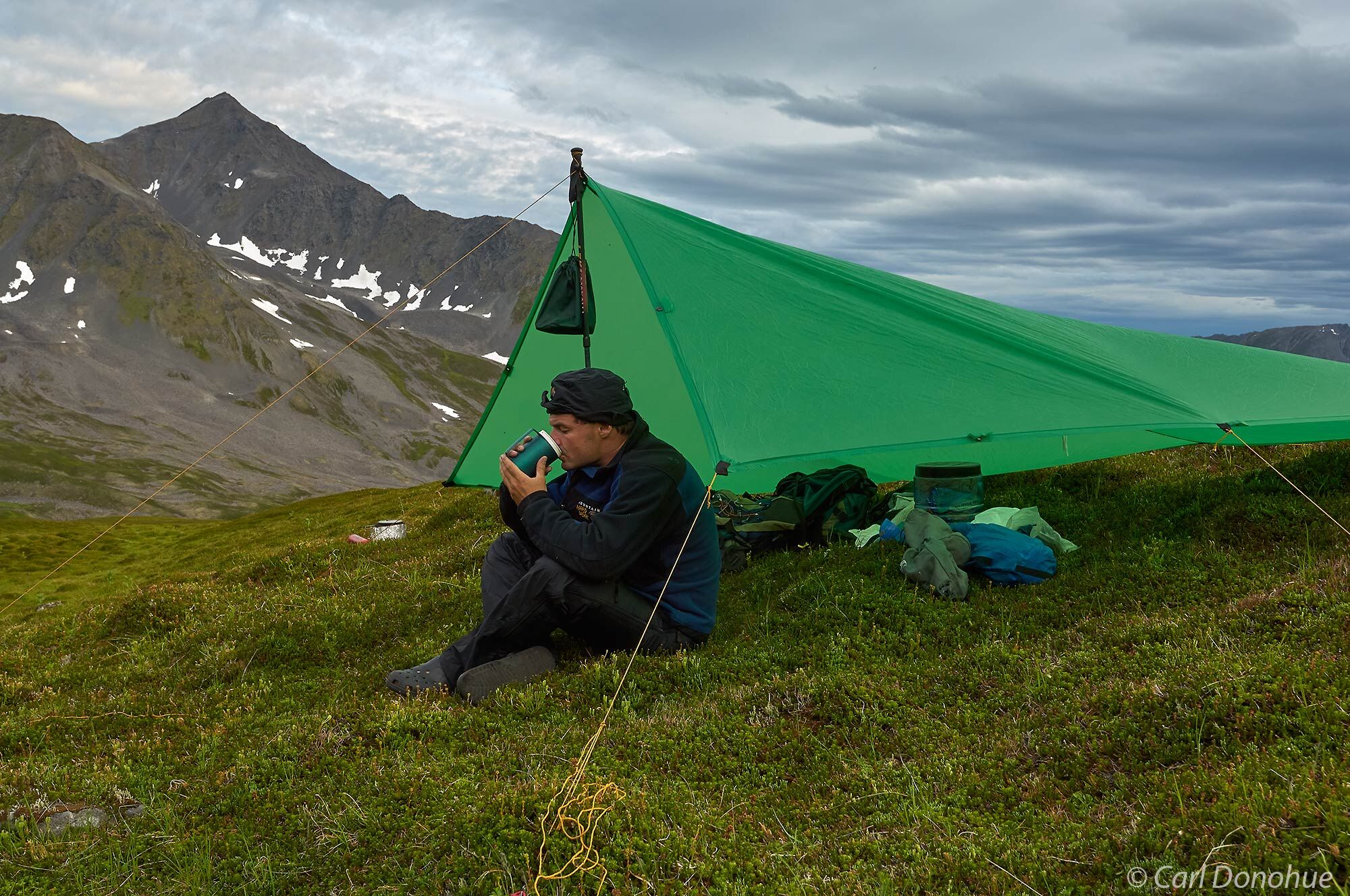 A backpacker eating dinner under a tarp in Denali National Park and Preserve